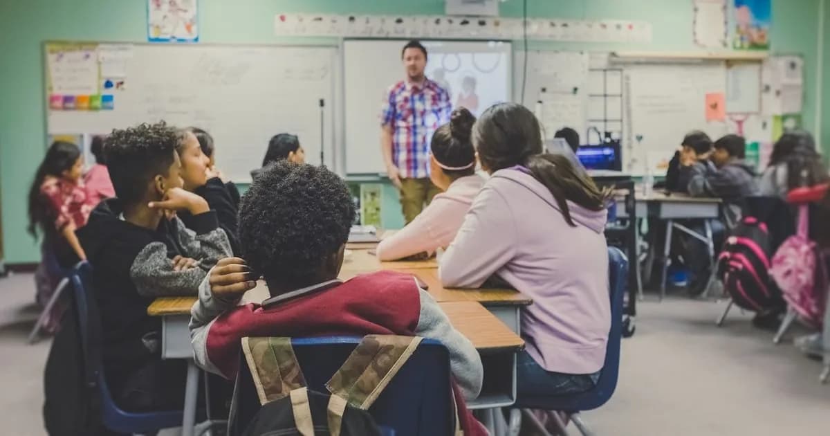 Professor conduz aula para turma diante do quadro em sala de aula de ensino fundamental