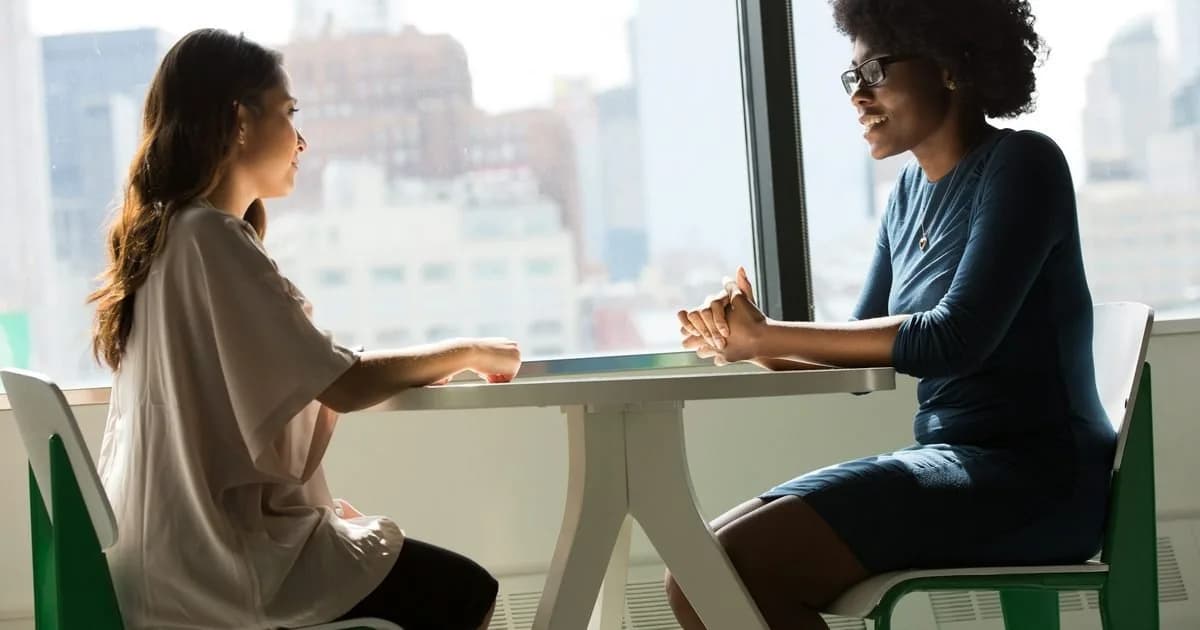 Duas profissionais de gestão de pessoas conversando em escritório com vista para a cidade