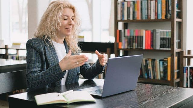 Mulher sorrindo em videochamada pelo laptop em uma biblioteca