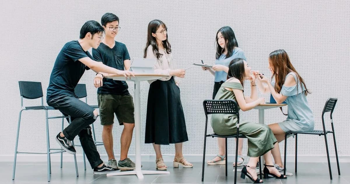 Grupo de estudantes discute em pé ao redor de mesas altas com tablet, em atividade de metodologia ativa