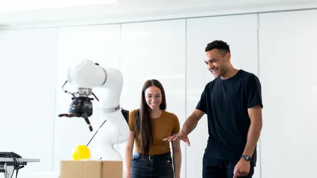 Engenheira e engenheiro conversando ao lado de um braço robótico em um laboratório