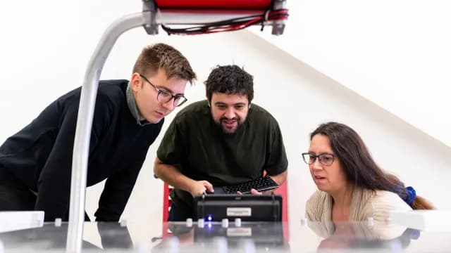 Três engenheiros testando juntos um equipamento eletrônico no laboratório