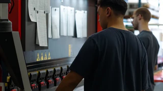 Dois operadores trabalhando em uma máquina de dobra em uma fábrica