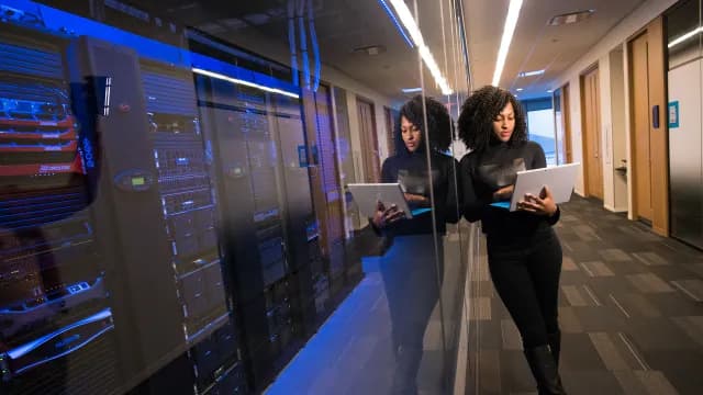 Engenheira de sistemas com notebook no corredor de um data center