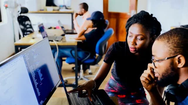 Dupla de desenvolvedores analisando código juntos em frente ao monitor, em um escritório de tecnologia