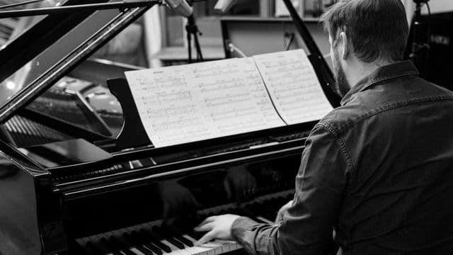 Músico ao piano lendo partitura de arranjo em estúdio de gravação