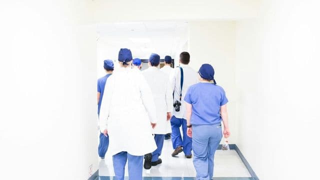 Equipe multiprofissional de saúde caminha por corredor claro de hospital