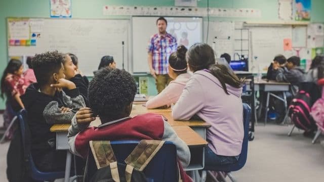 Professor conduz aula para turma diante do quadro em sala de aula de ensino fundamental