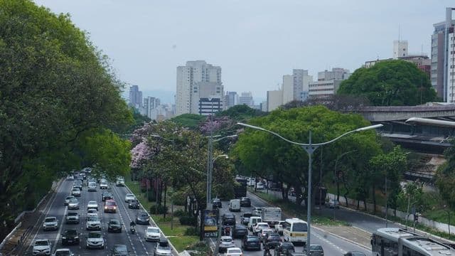 Avenida movimentada de São Paulo com trânsito intenso de carros e ônibus e prédios ao fundo