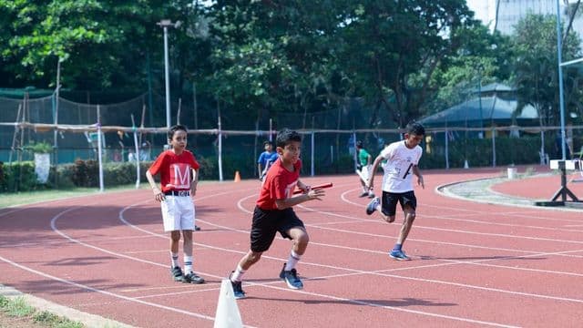 Alunos correm em revezamento numa pista de atletismo escolar durante aula de educação física