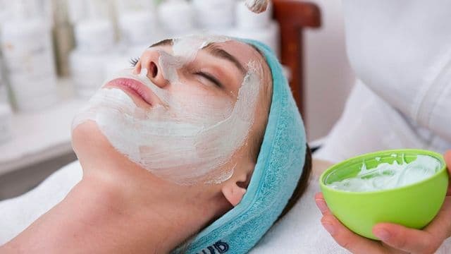 Profissional de estética aplicando máscara facial em cliente, representando a pós em Estética Facial e Corporal Avançada da UFEM