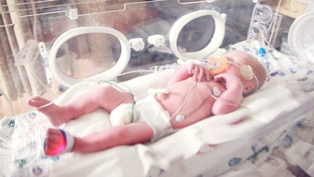 Bebê prematuro em incubadora na UTI neonatal, com sensores e suporte respiratório, cenário de atuação da fisioterapia neonatal
