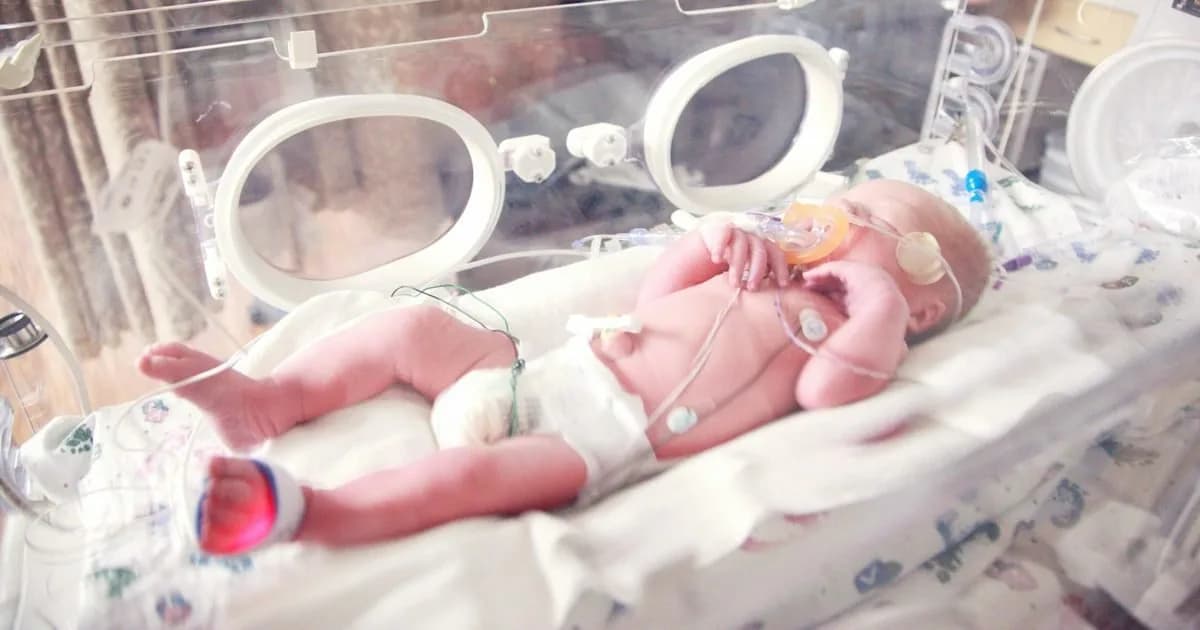 Bebê prematuro em incubadora na UTI neonatal, com sensores e suporte respiratório, cenário de atuação da fisioterapia neonatal