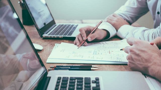 Dois profissionais analisam documento de planejamento sobre a mesa entre notebooks em escritório