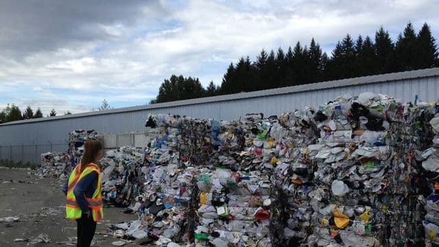 Profissional com colete de segurança observando fardos de material reciclado em centro de triagem de resíduos