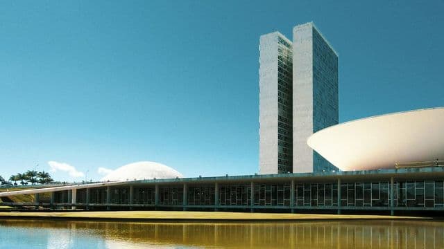 Congresso Nacional em Brasília com as duas torres e as cúpulas refletidas no espelho d'água em dia claro