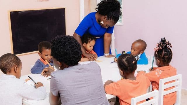 Professora orienta criancas em atividade de desenho em sala de educacao infantil colorida