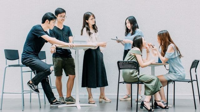 Grupo de estudantes discute em pé ao redor de mesas altas com tablet, em atividade de metodologia ativa