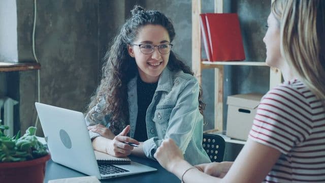 Duas profissionais conversando durante atendimento de orientação social, simbolizando o trabalho de direitos humanos e ressocialização