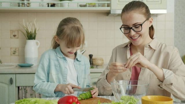 Mãe e filha preparam salada juntas na cozinha, simbolizando a nutrição pediátrica e o combate à obesidade infantil