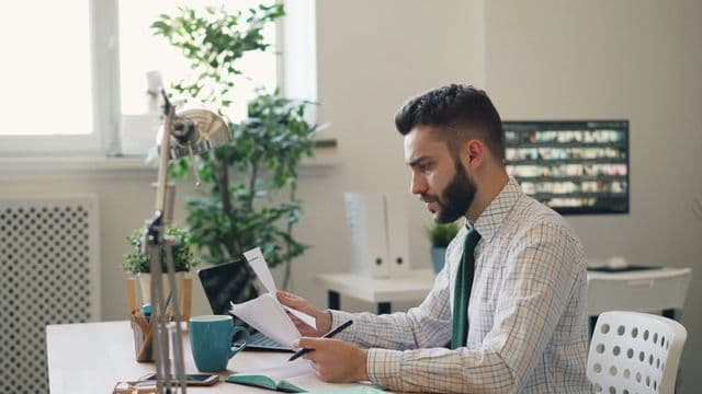 Perito revisando documentos financeiros e laudos periciais em escritório