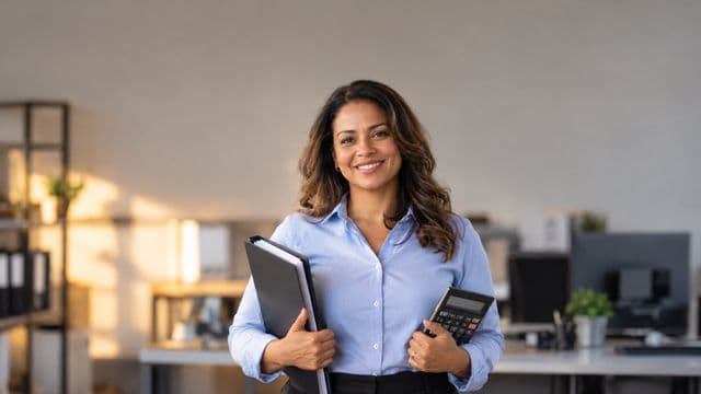 Contadora sorrindo, com camisa social azul-clara, segurando uma calculadora e uma pasta de documentos, em um escritório contábil moderno