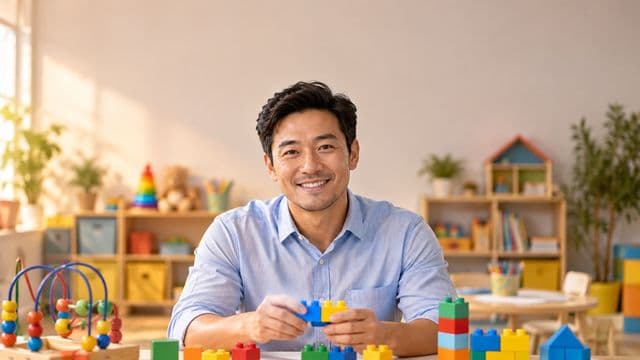 Psicopedagogo sorrindo, com camisa azul-clara, segurando blocos de montar coloridos, em uma sala de atendimento infantil colorida e organizada, com brinquedos pedagógicos