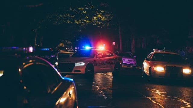 Viaturas de polícia com giroflex ligado em rua à noite, cenário do trabalho de segurança pública e inteligência
